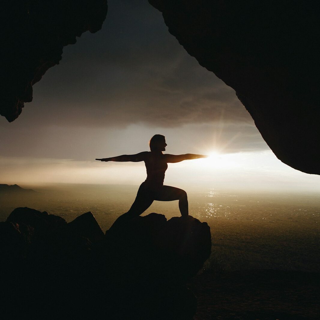 silhouette of person in yoga post on top of cliff during sunset